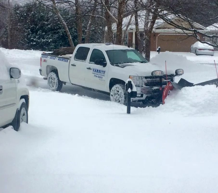 White pickup truck with a snowplow pushing snow on a snowy residential street