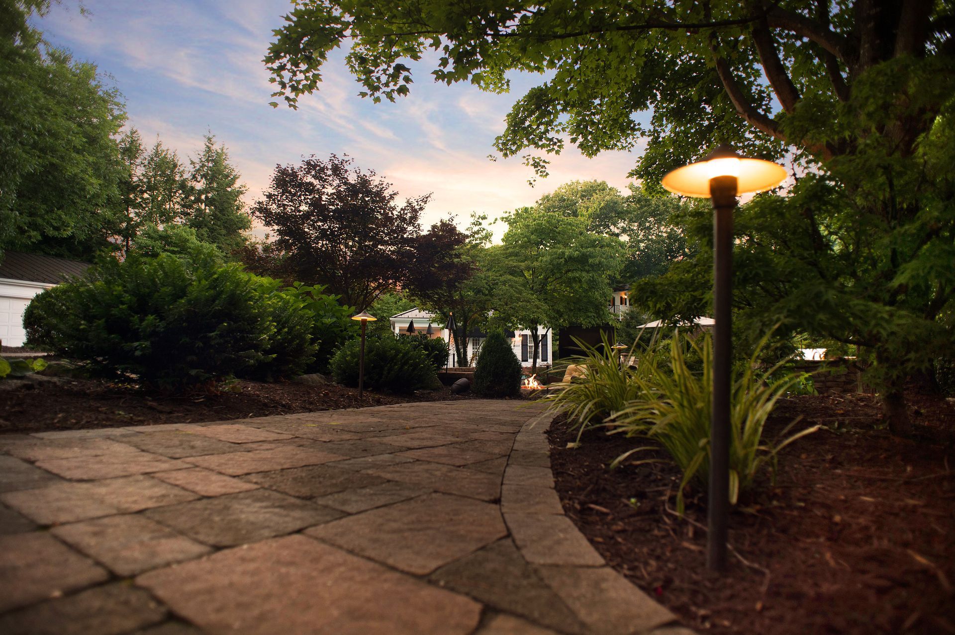 Stone patio with a circular fire pit burning beside a calm lake and boathouse.