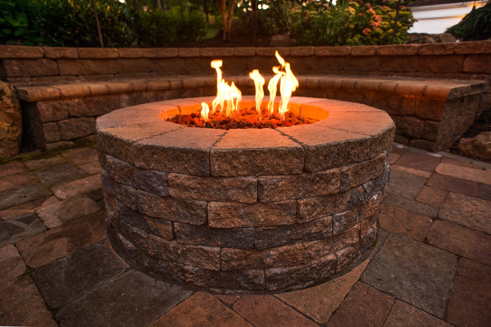 Stone fire pit with flames burning in a circular courtyard at dusk