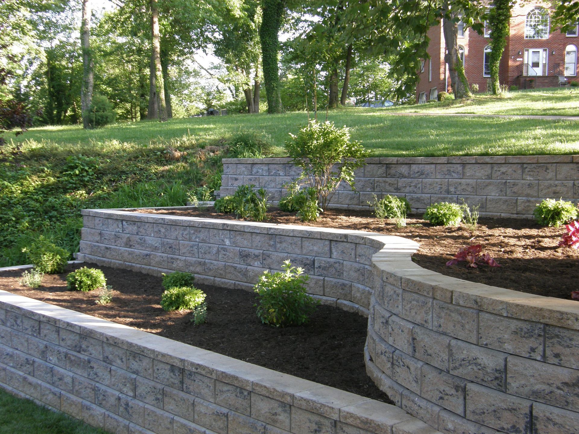 Tiered stone garden terraces with small shrubs and flowers in a leafy park setting