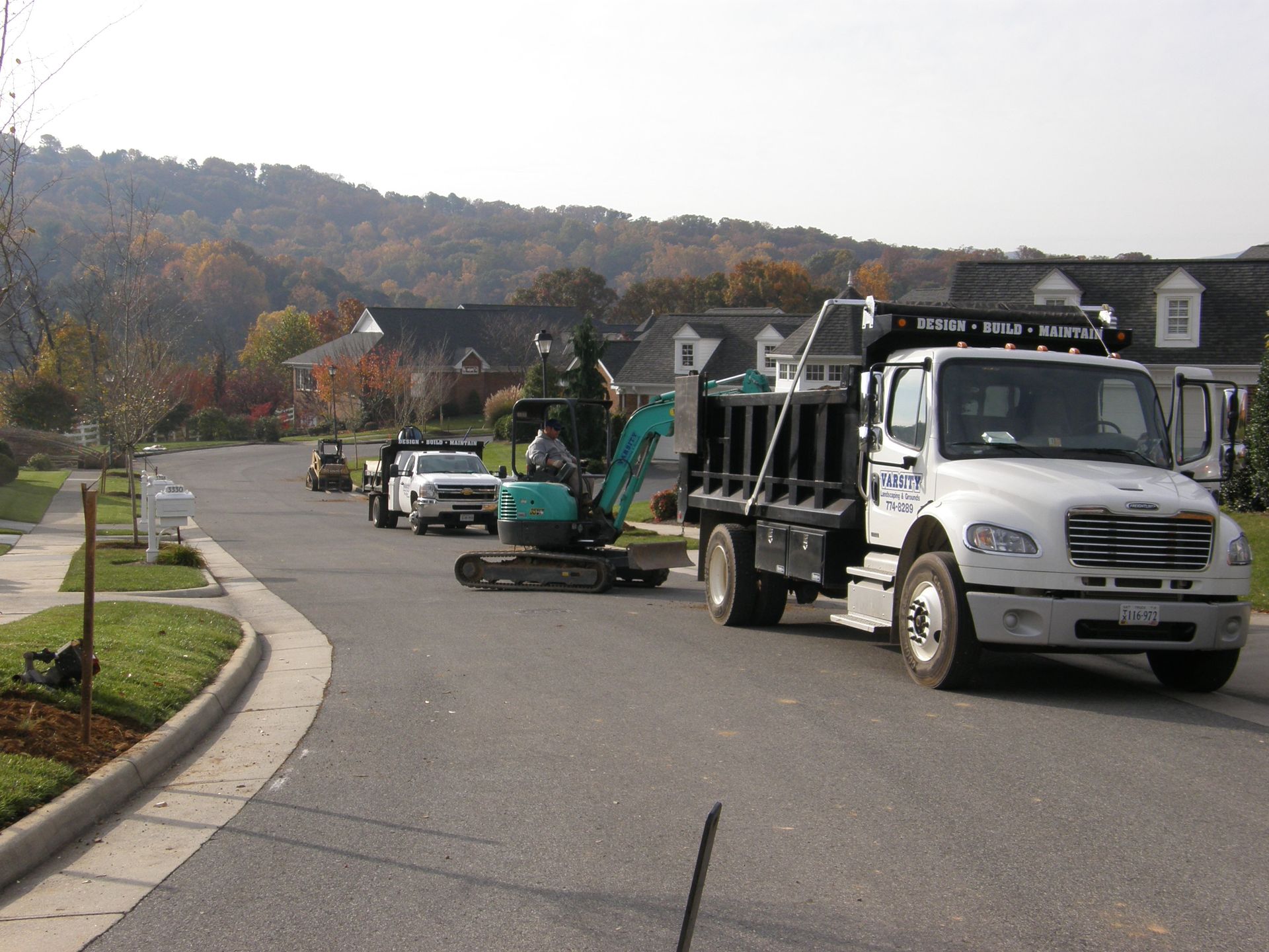 Landscape trucks and construction equipment parked on a quiet suburban street.