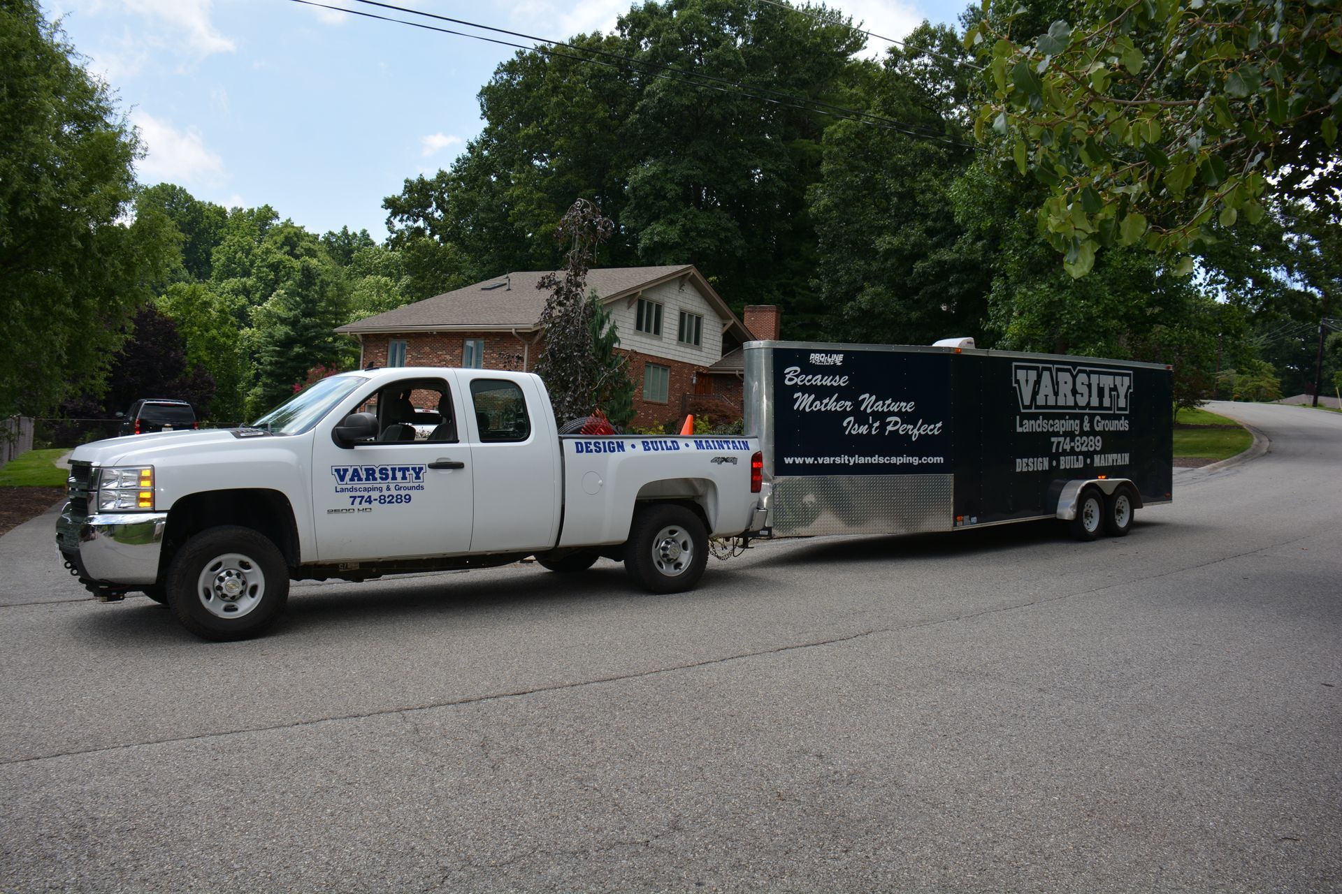 White pickup truck towing a black trailer on a tree-lined residential street