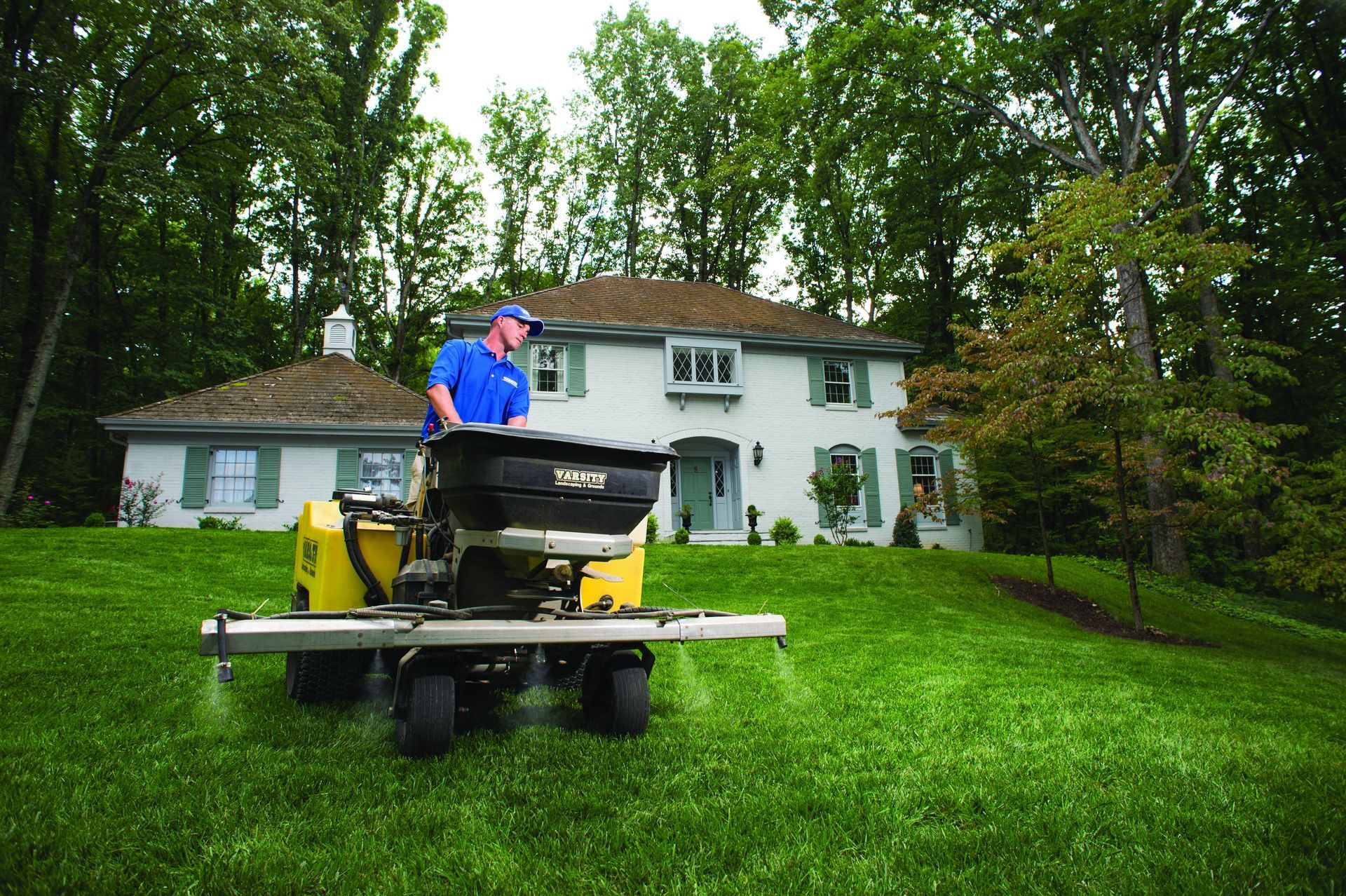 Man mowing a lush green lawn in front of a white house with a yellow riding mower