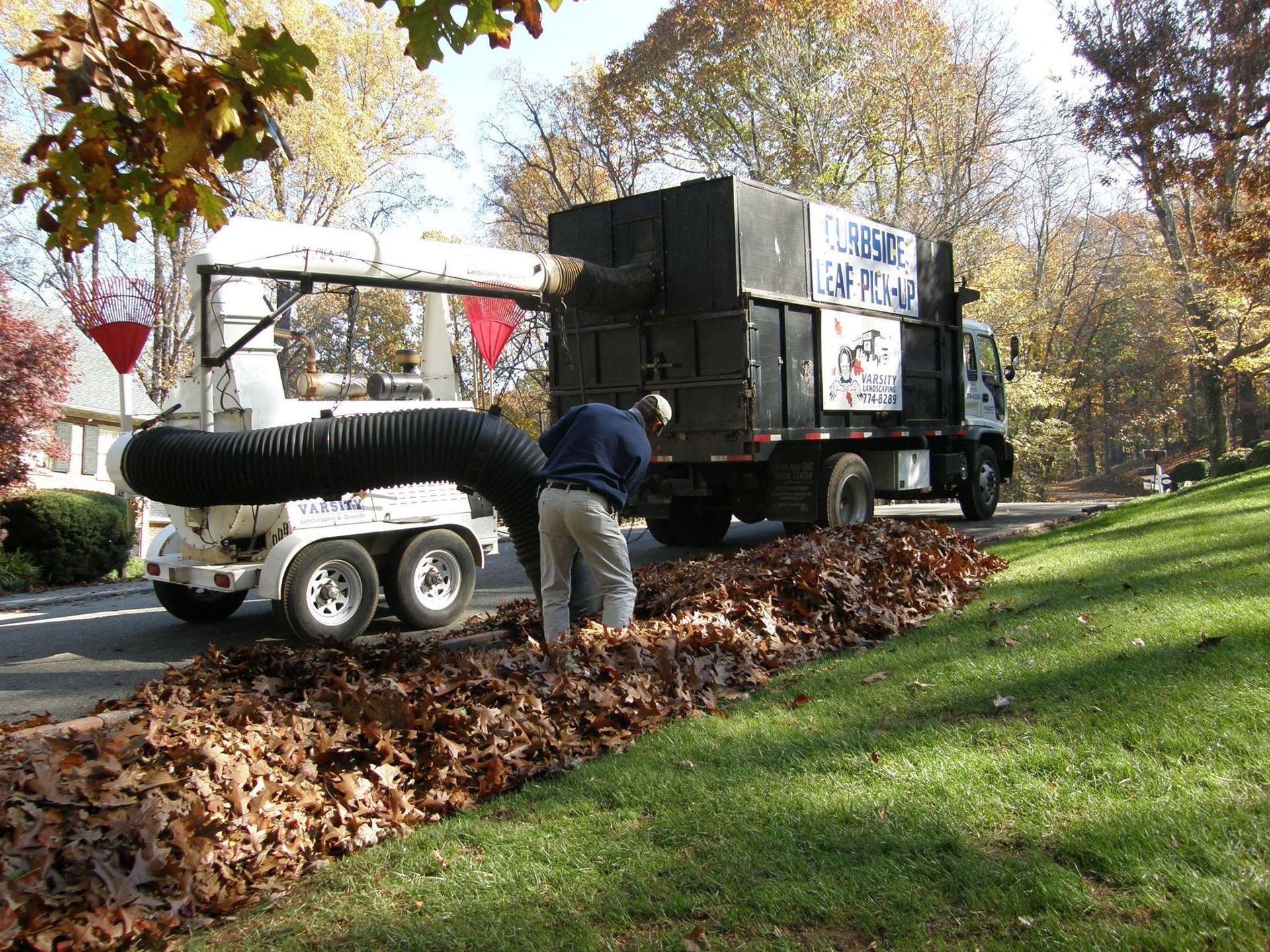 Truck unloading leaves into a trailer beside a park path in autumn