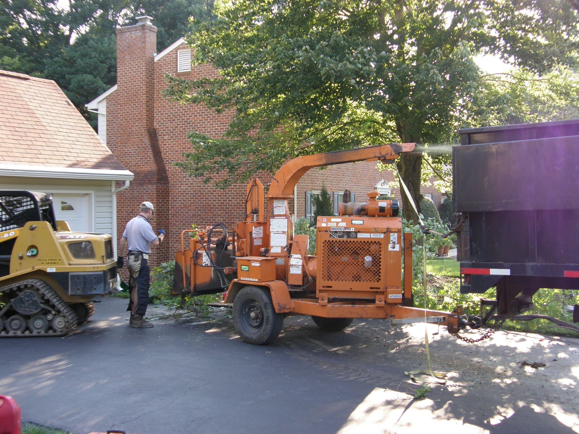 Orange wood chipper and workers outside a house beside a large purple truck