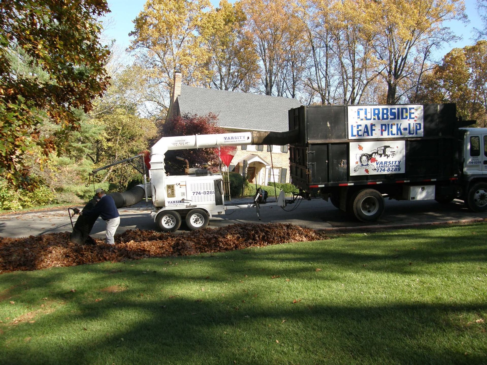 Workers loading leaves into a truck in a park during autumn