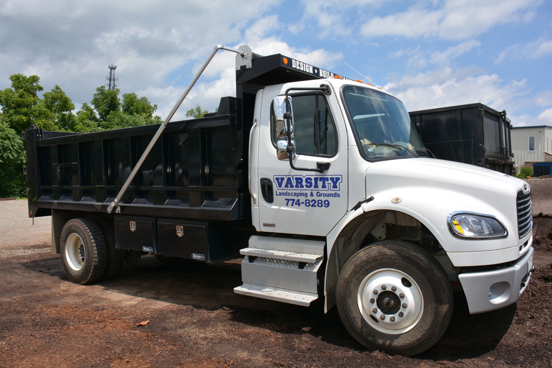 White and black dump truck parked on a gravel lot with “VARSITY” on the door