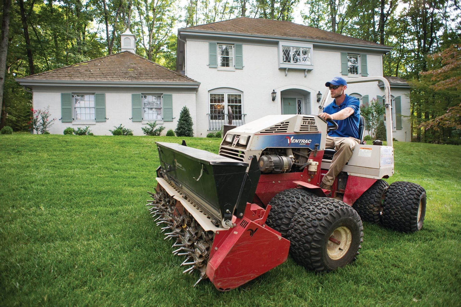 Gardener edging a lawn beside blooming red flowers, using a hose in a sunny yard