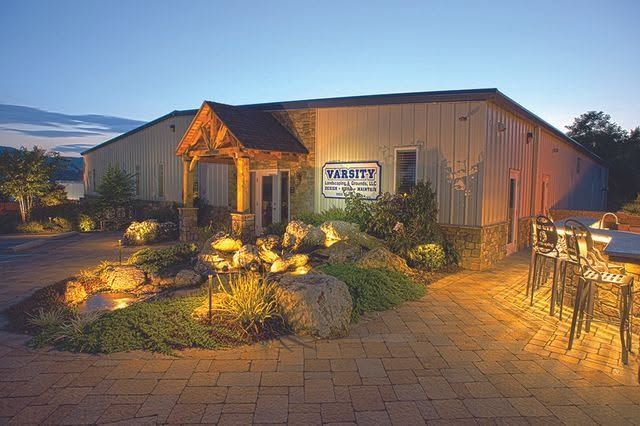 Outdoor restaurant entrance at dusk with warm lights, stone landscaping, and patio seating by a metal-sided building.
