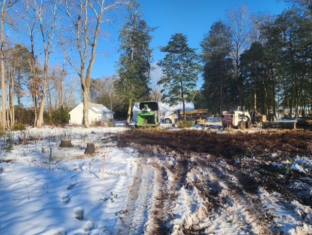 A green tractor is driving through a snowy field.