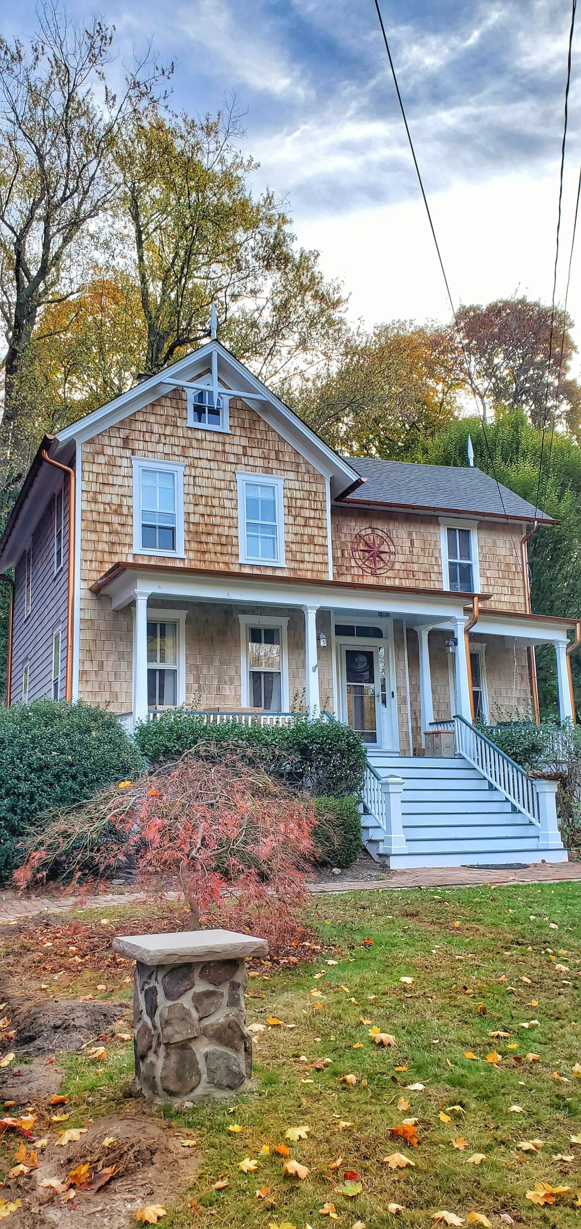 A large stone house with a porch and stairs in the middle of a lush green field.