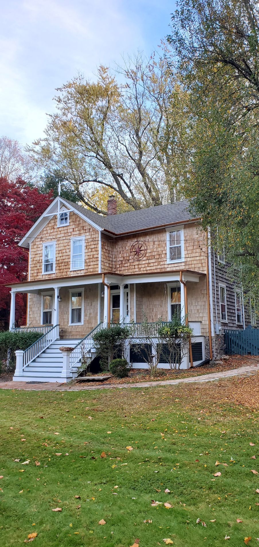 A large house with a large porch is sitting on top of a lush green field.