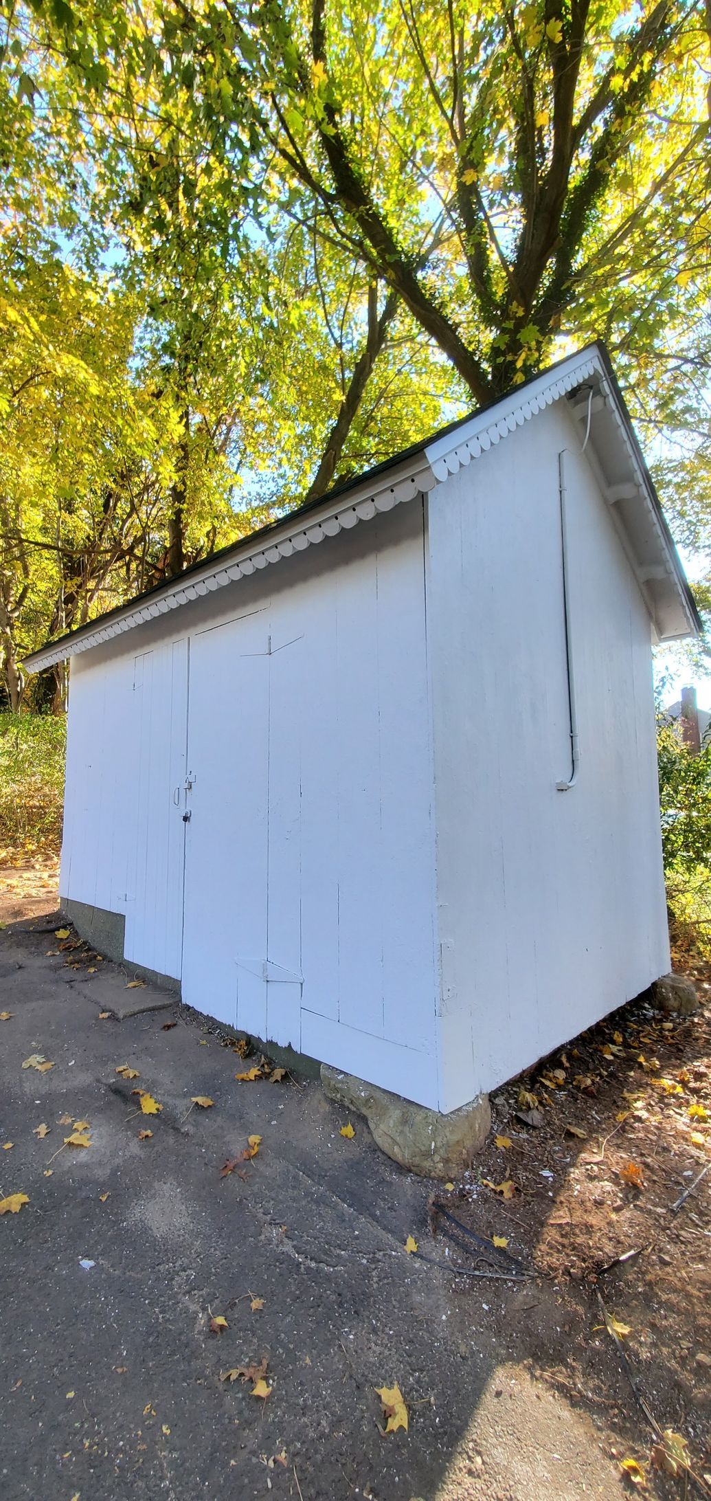 A small white shed is sitting on the side of a road next to a tree.