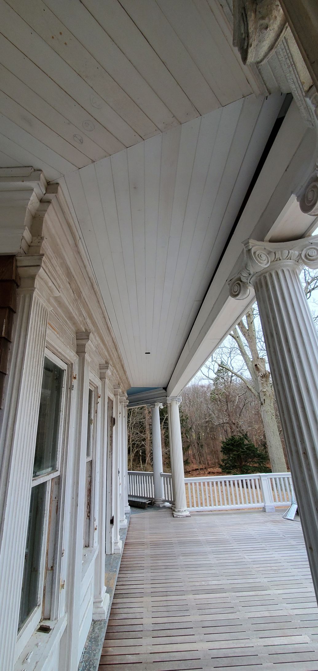 A long white porch with columns and a car parked on the side of it.