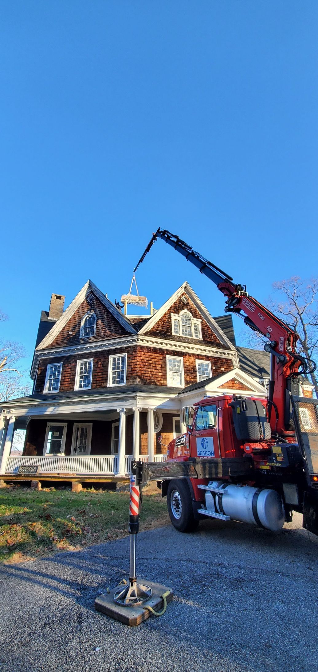 A red truck with a crane attached to it is parked in front of a large house.