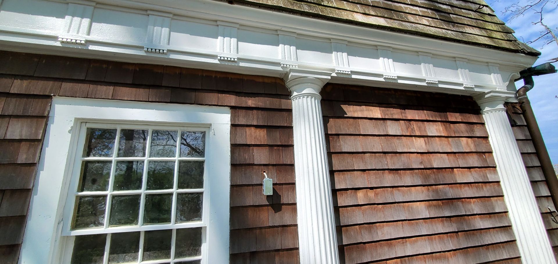 A house with wooden siding and white columns has two windows and a porch.