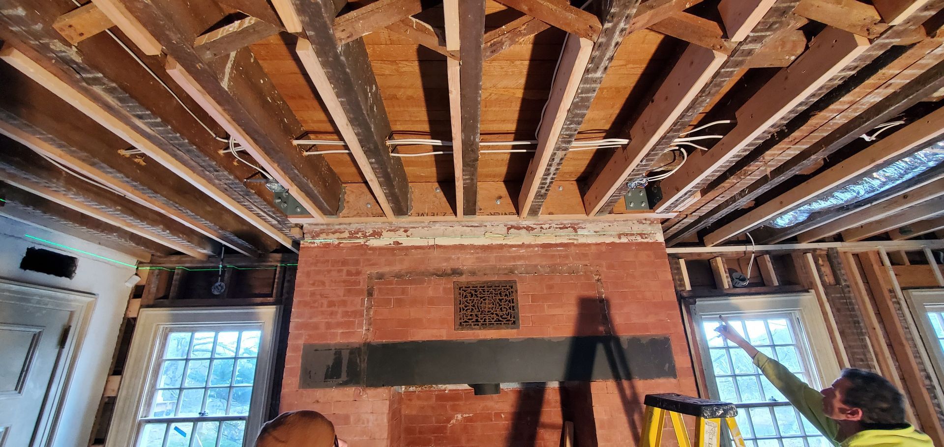 A man is standing on a ladder in a room with a brick fireplace.