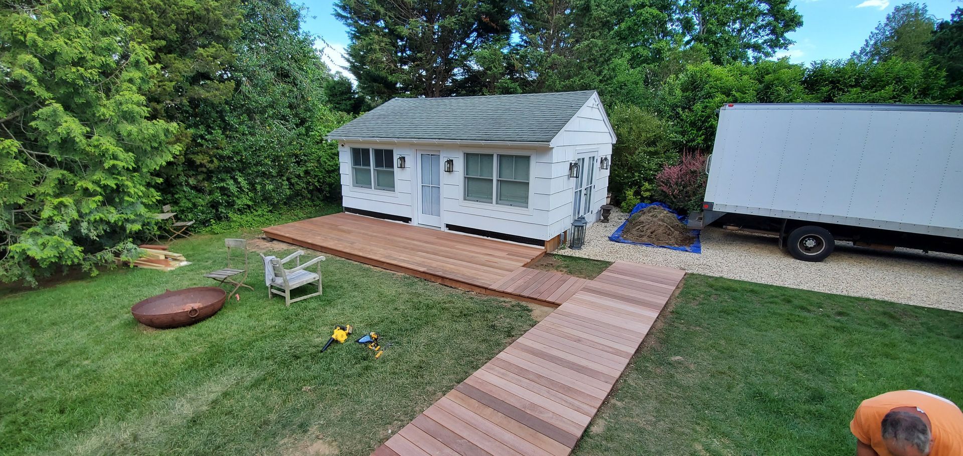 A man is standing in front of a small white house in a backyard