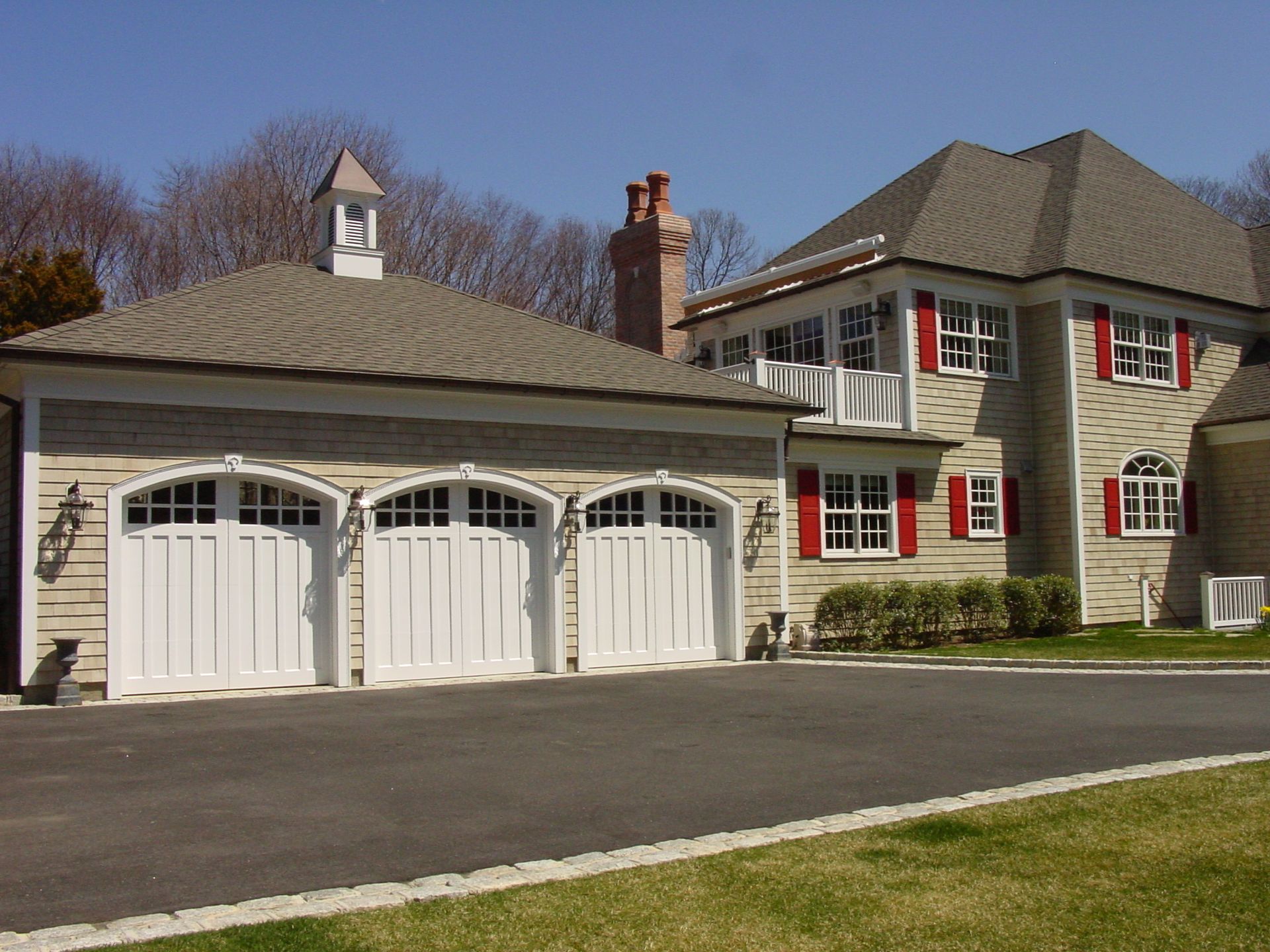 A large house with three garage doors and red shutters