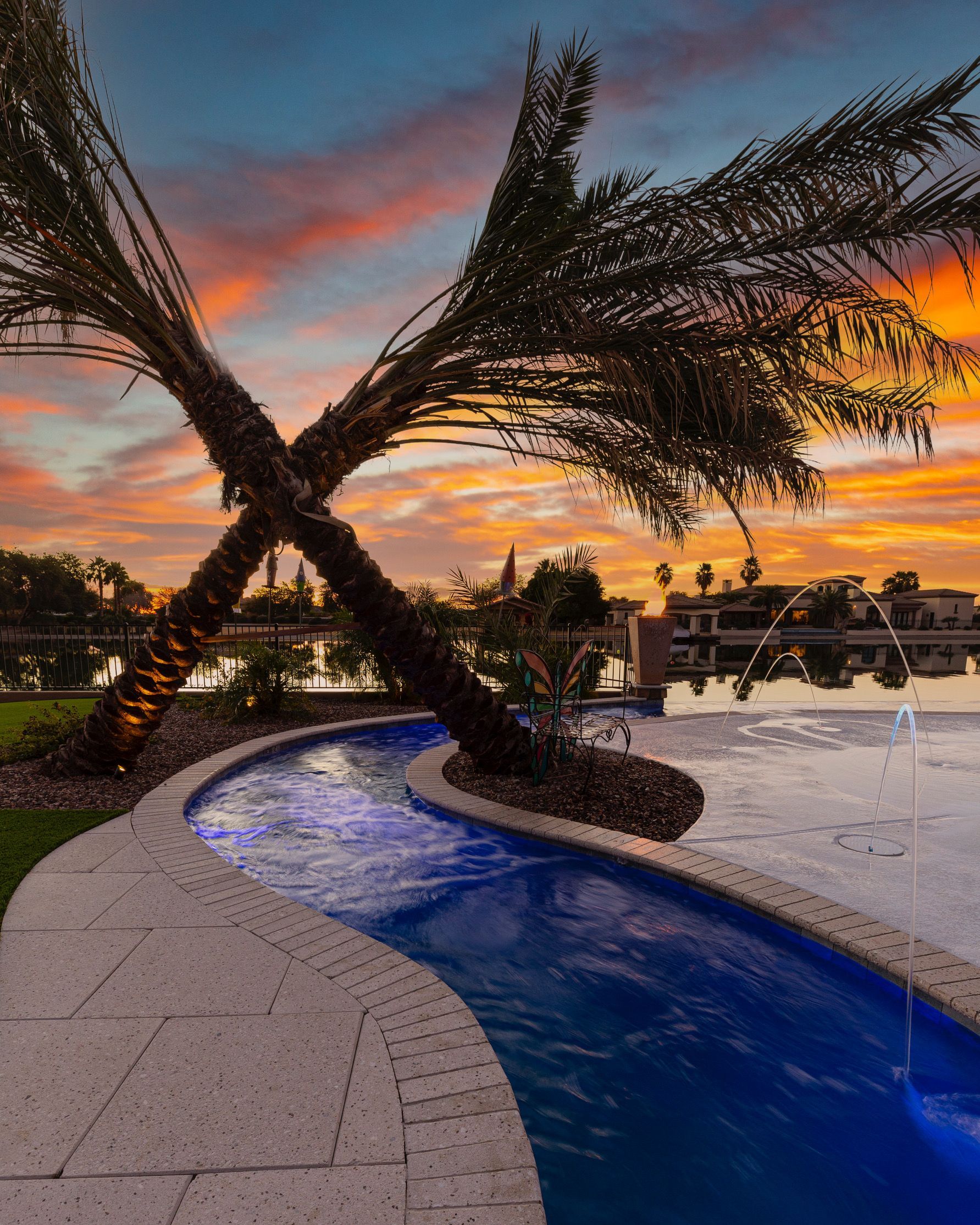 A swimming pool with a waterfall and palm trees in the background at sunset.