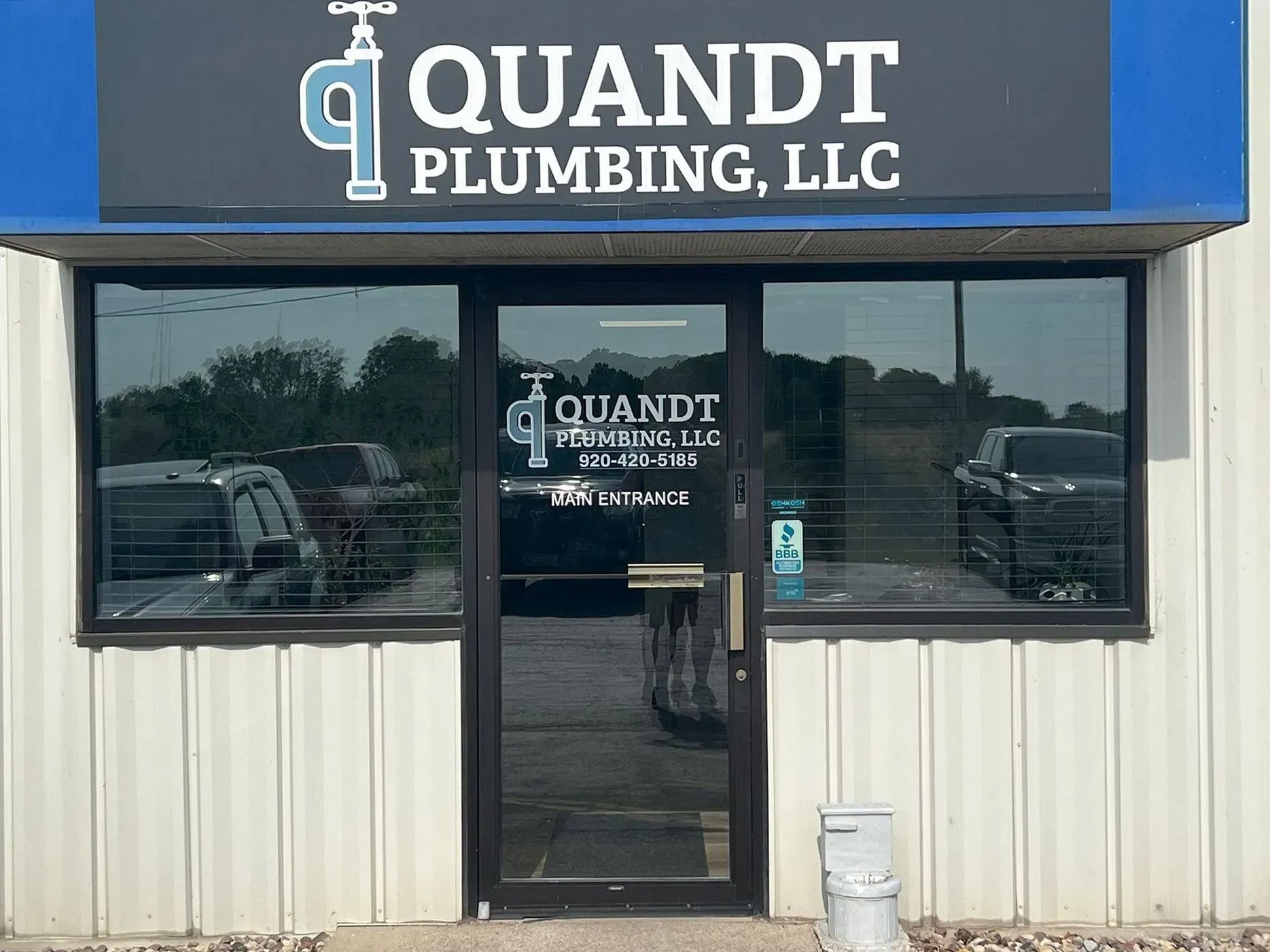Quandt Plumbing, LLC storefront with logo above the entrance. Dark tinted windows, vehicles visible.