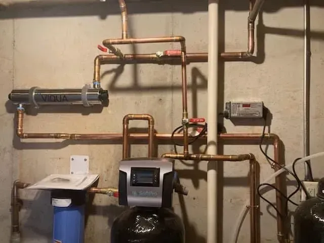 Copper pipes and water filtration system in a basement setting.