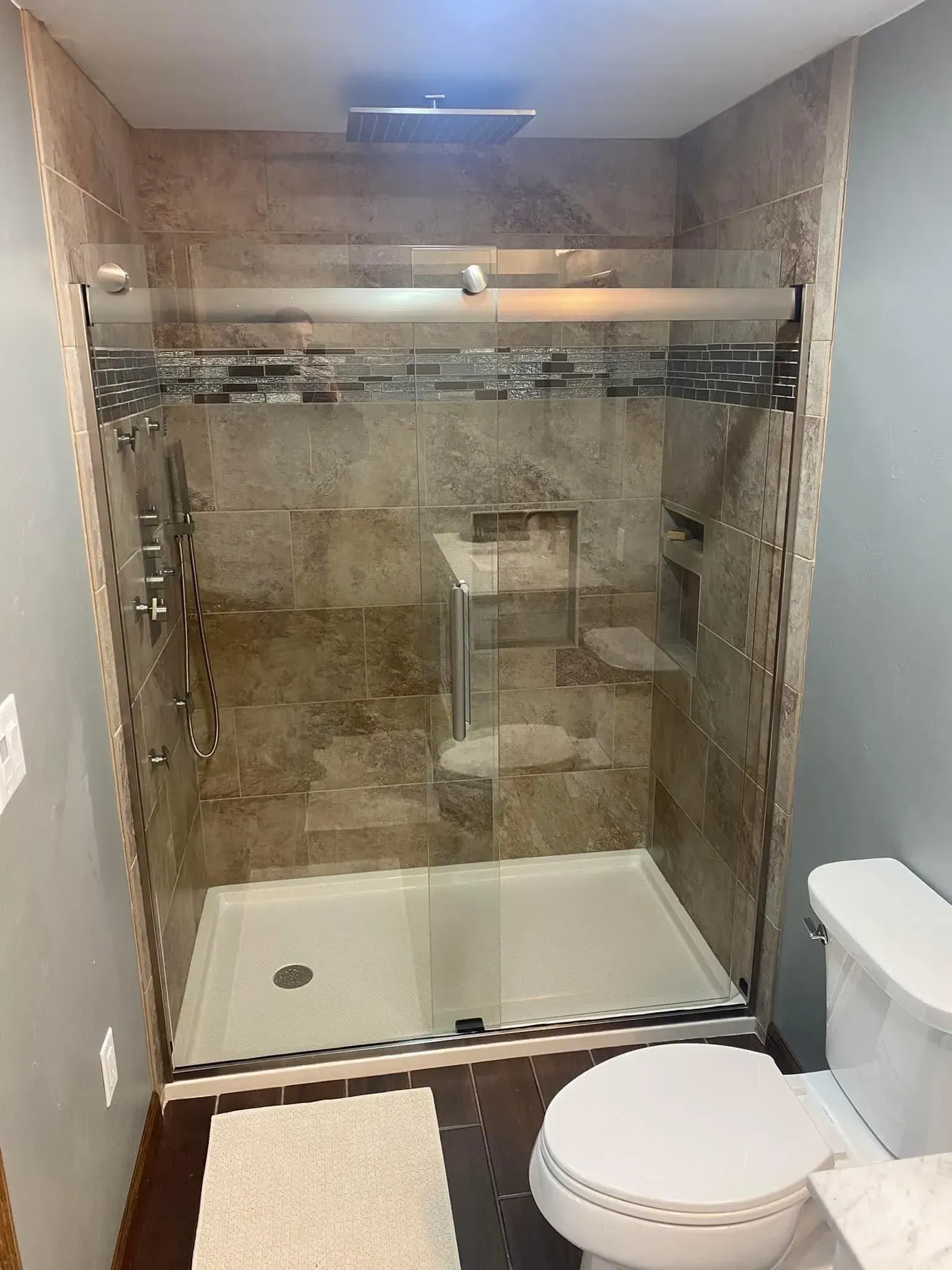 Modern bathroom with a glass shower, beige tile, and a white toilet.