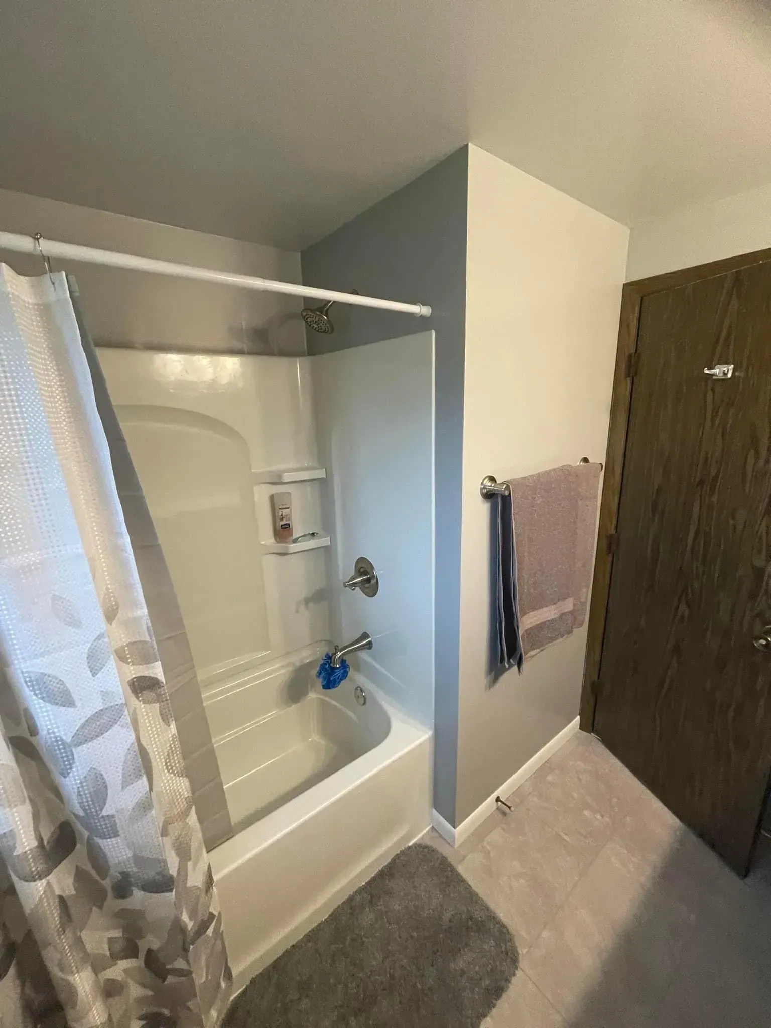 Bathroom with a white tub, gray walls, and a towel rack with a towel.