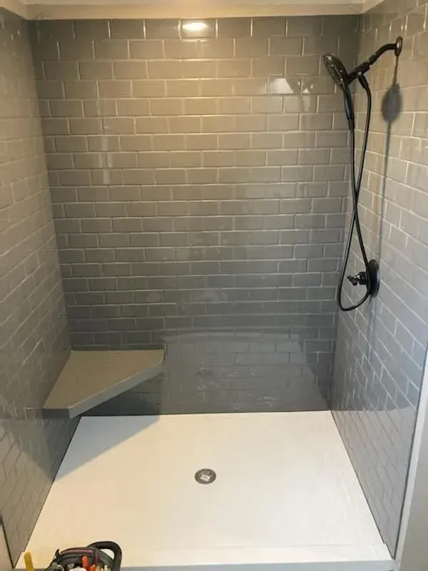 Gray tiled shower with a white base and a corner seat; black shower fixtures.