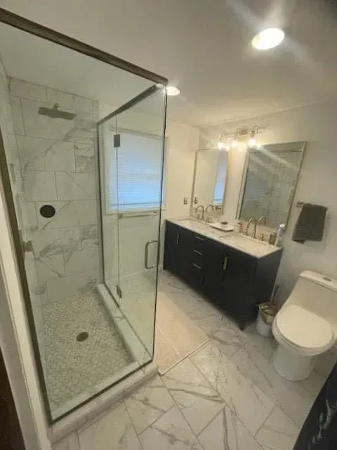Modern bathroom with marble tile, glass shower, black vanity, and white toilet.