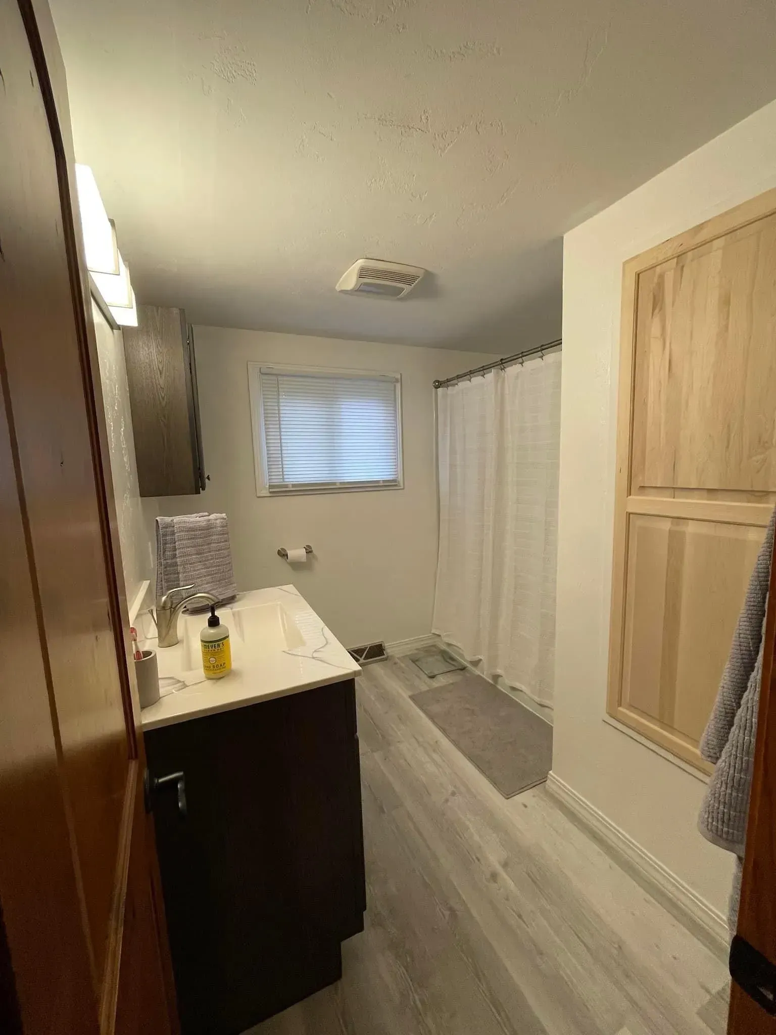 Bathroom with a dark vanity, window, shower curtain, and light-colored flooring and walls.