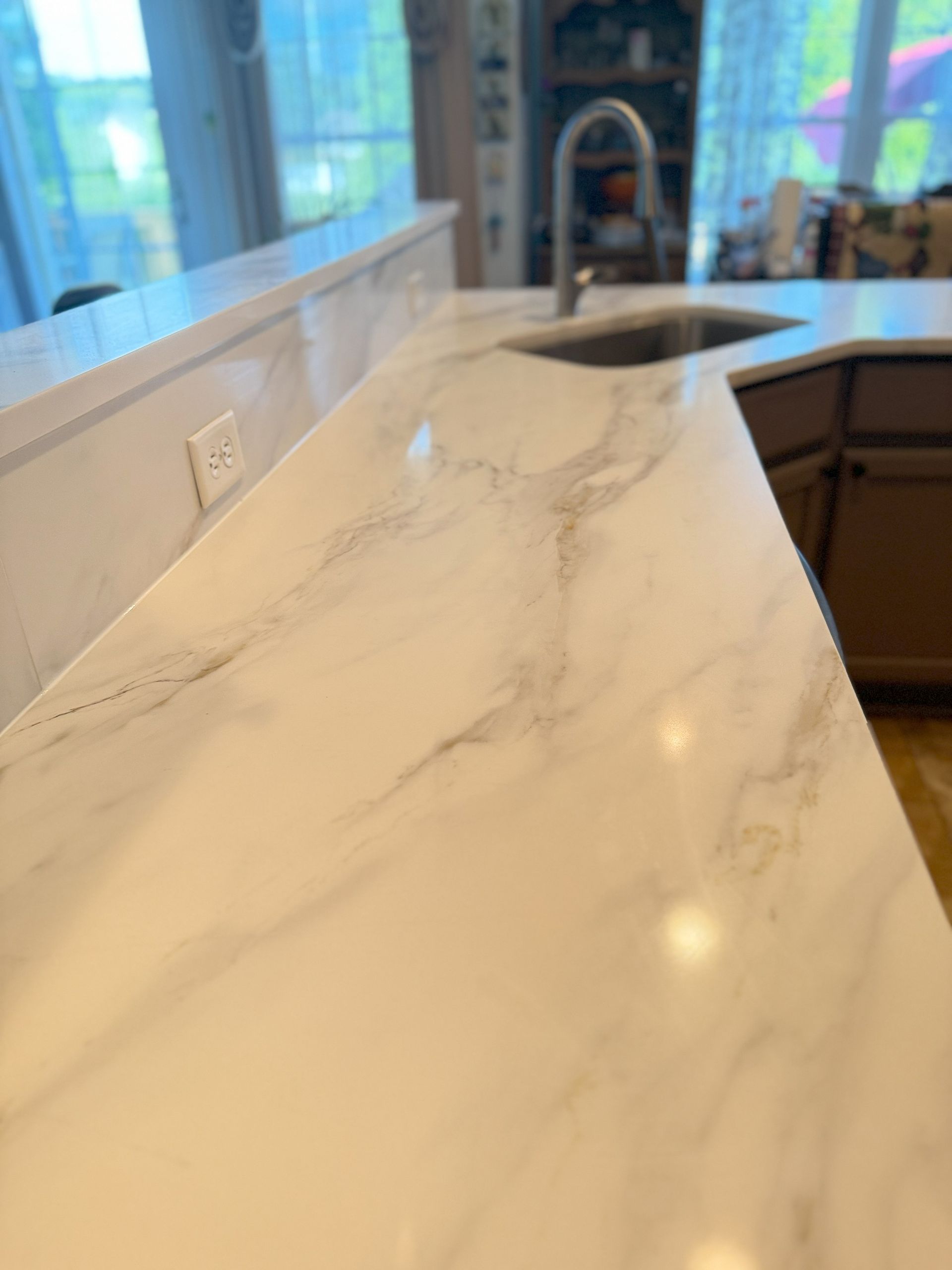White marble-look kitchen countertop with a sink and faucet, in a well-lit modern kitchen.