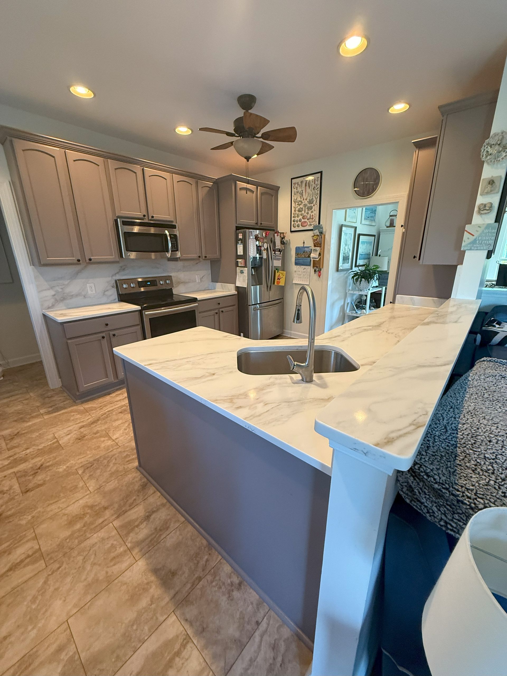 Kitchen with gray cabinets, white countertops, island with a sink, and stainless steel appliances.