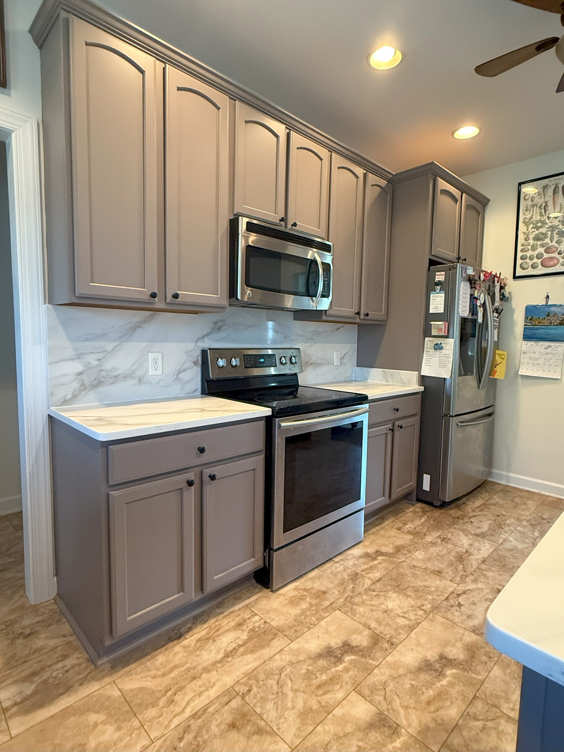 Gray kitchen cabinets, stainless steel appliances, white countertops, and patterned beige floor.