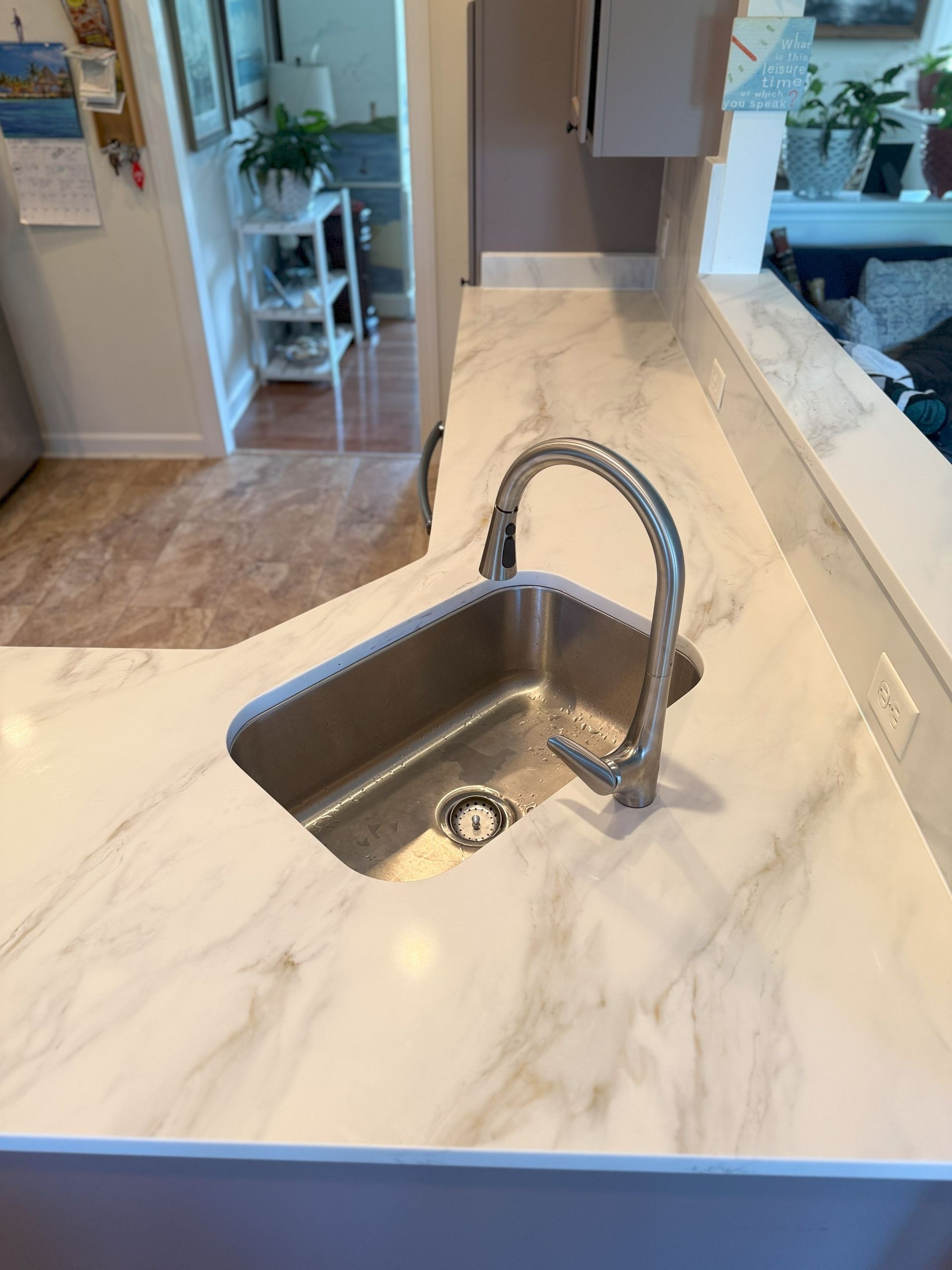 Stainless steel kitchen sink with faucet on white marble-patterned countertop.