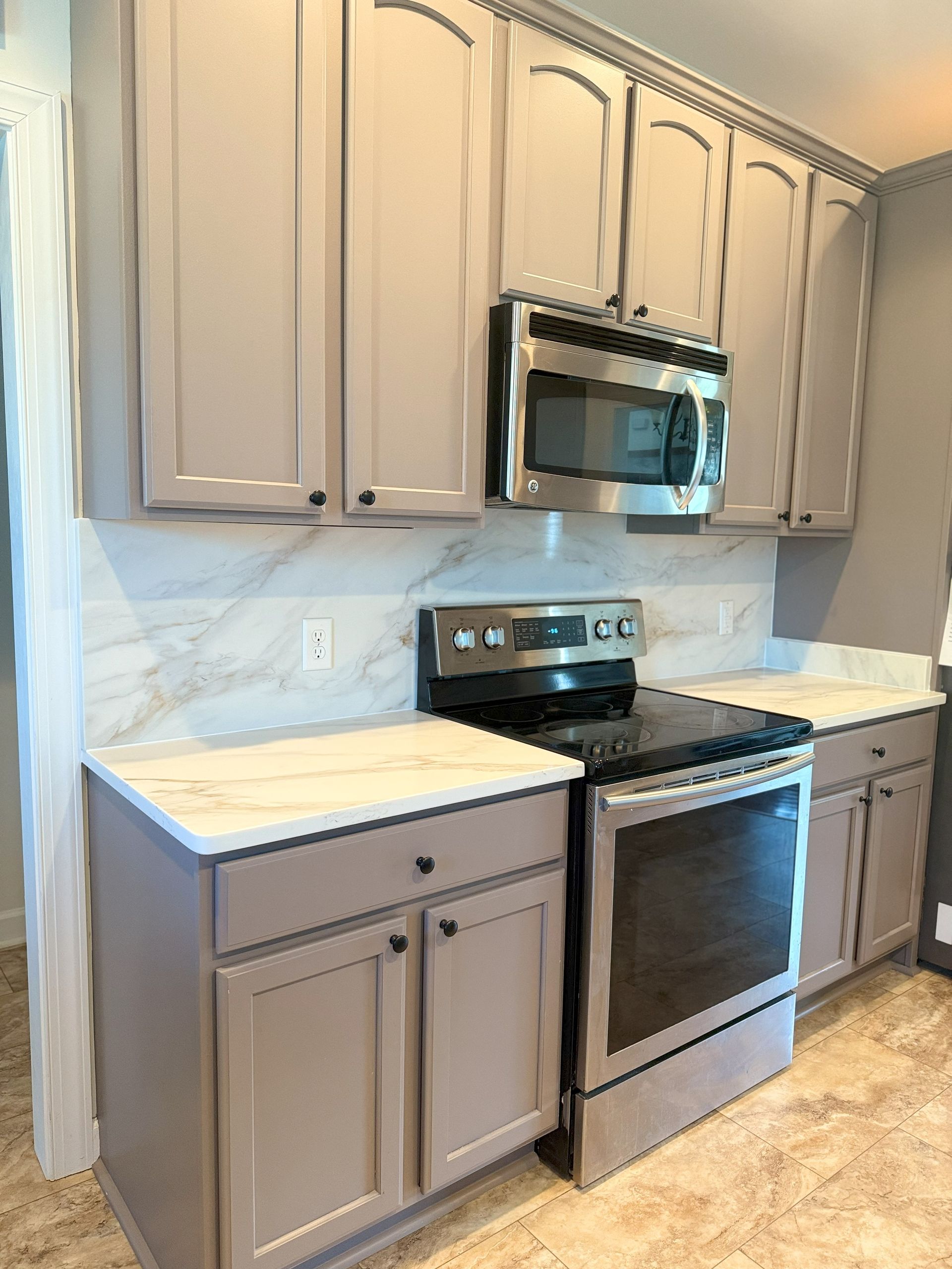 Kitchen with gray cabinets, white countertops, stainless steel appliances, and marble-look backsplash.