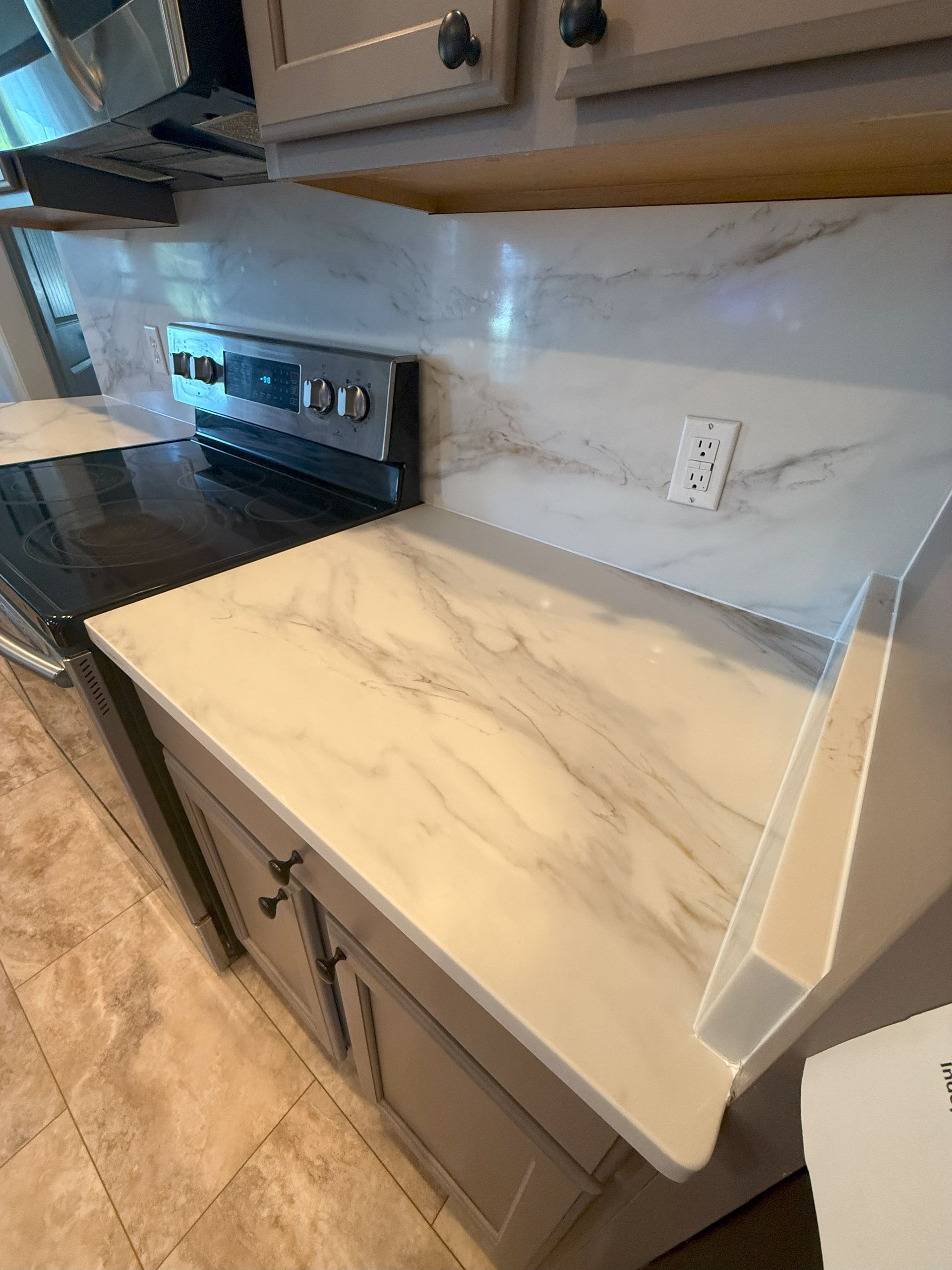 Kitchen counter with marble-like surface, stove, cabinets, and electrical outlet.