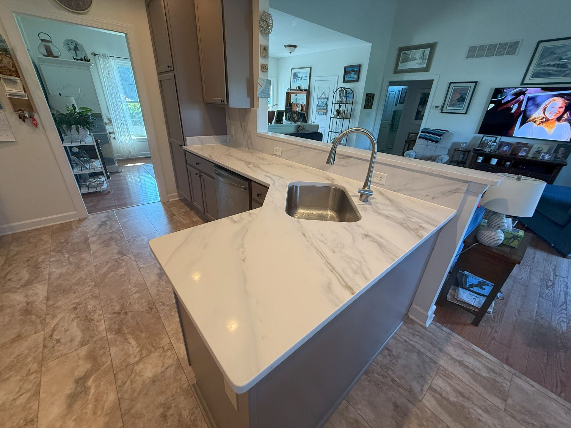 Kitchen island with white countertops, sink, and faucet; view into living area.