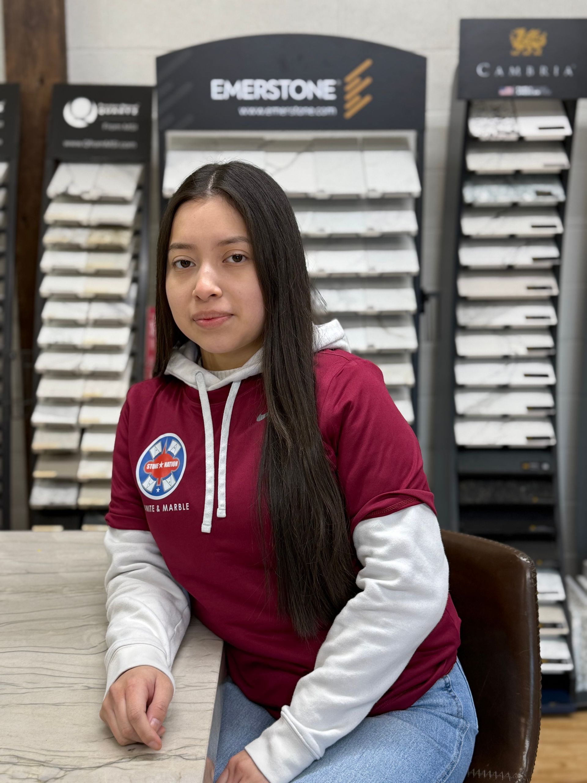 A woman in a maroon shirt is sitting in front of a counter in a store.