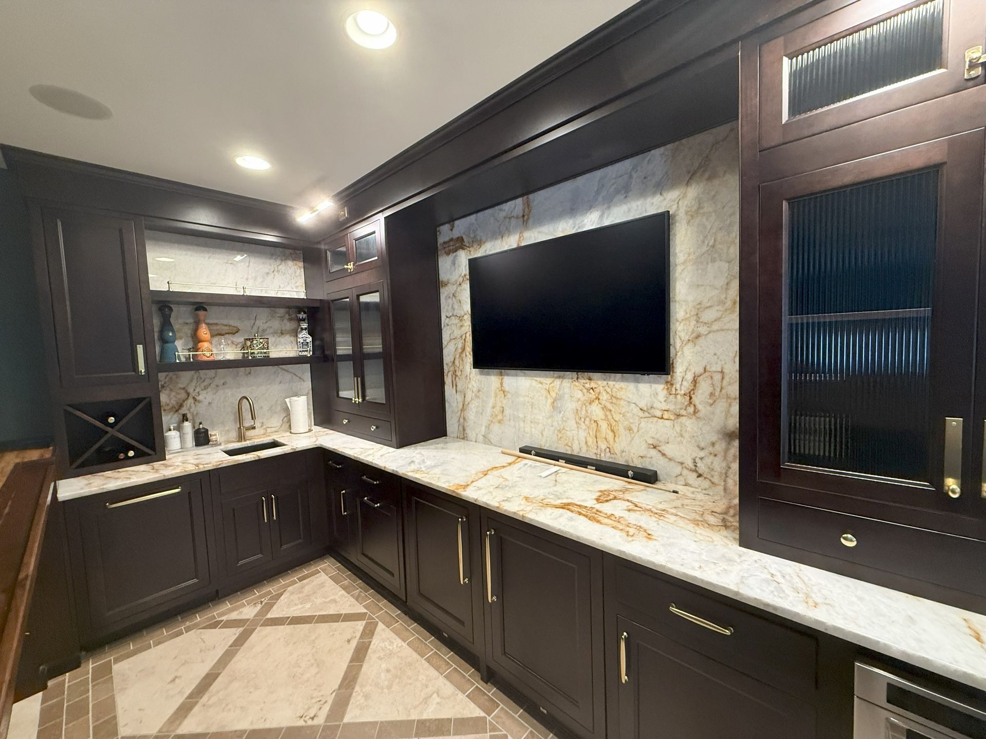 Dark wood home bar with a TV, granite countertop, and gold hardware.