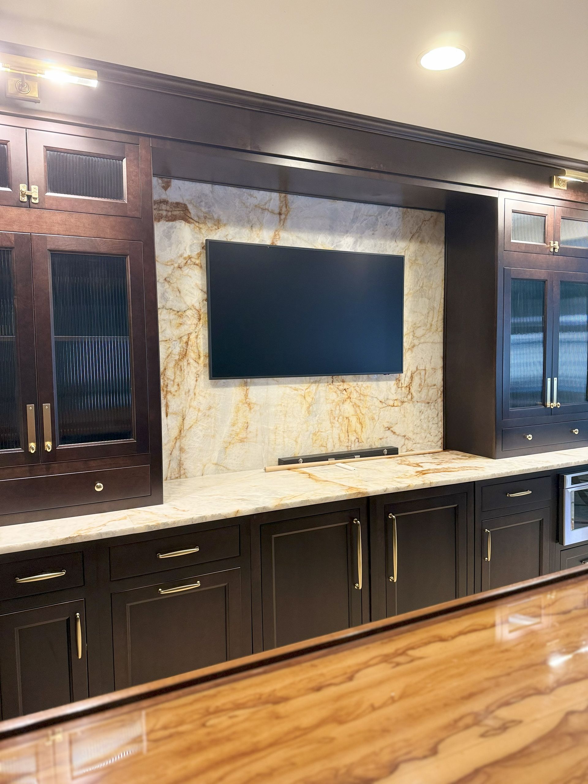 Dark wood entertainment center with TV on a stone backdrop, cabinets, and golden accents.