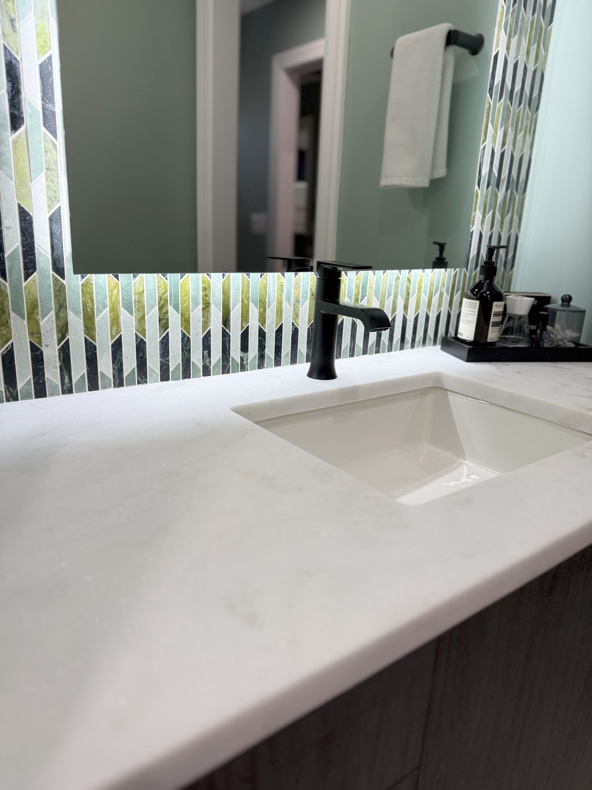 Bathroom vanity with white countertop, black faucet, and decorative mosaic tile.