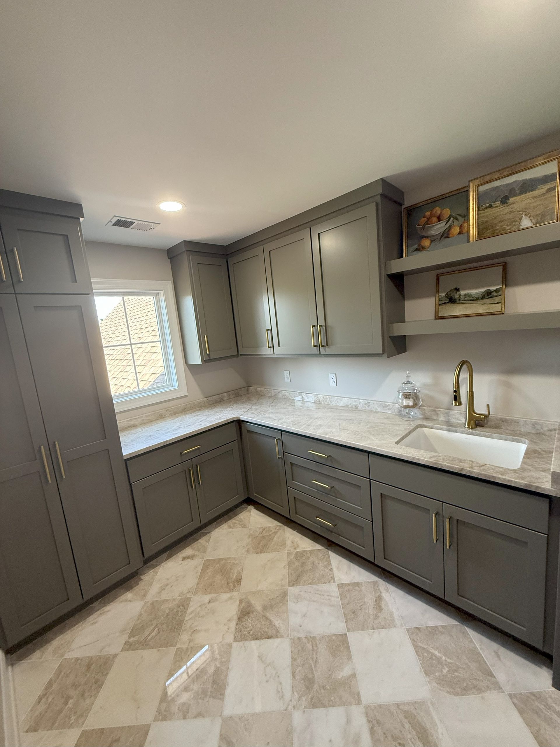 Gray kitchen cabinets with gold hardware and white countertops, checkered floors.