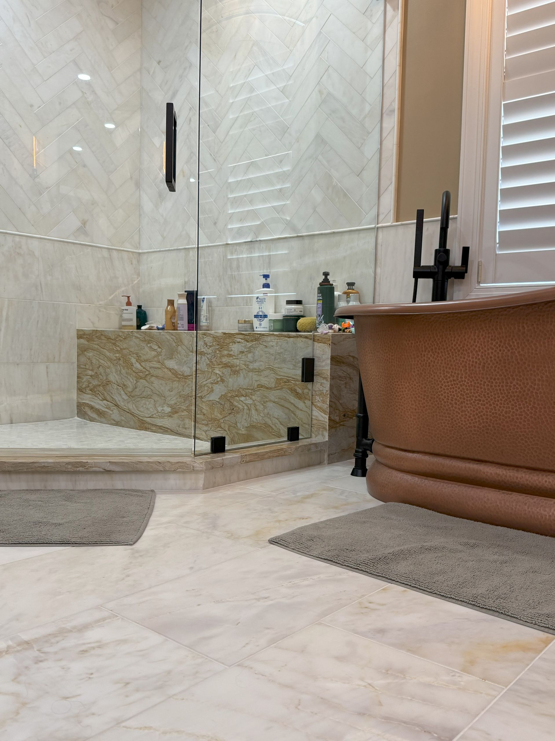 Luxurious bathroom with copper tub, glass shower, and light-colored marble tiles.