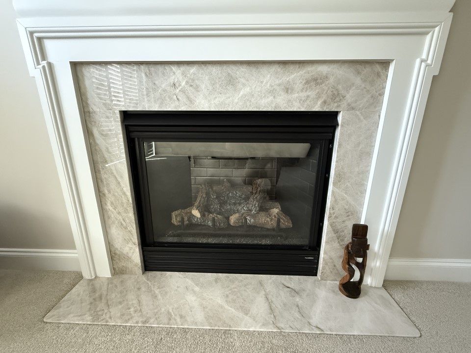 Fireplace with marble tile and black firebox, white mantel. Decorative wooden sculpture stands on hearth.