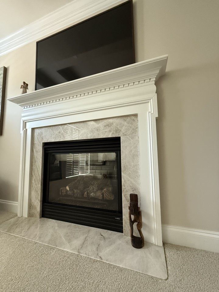 Fireplace with white mantel, marble surround, and TV above. Brown decorative object on the hearth.