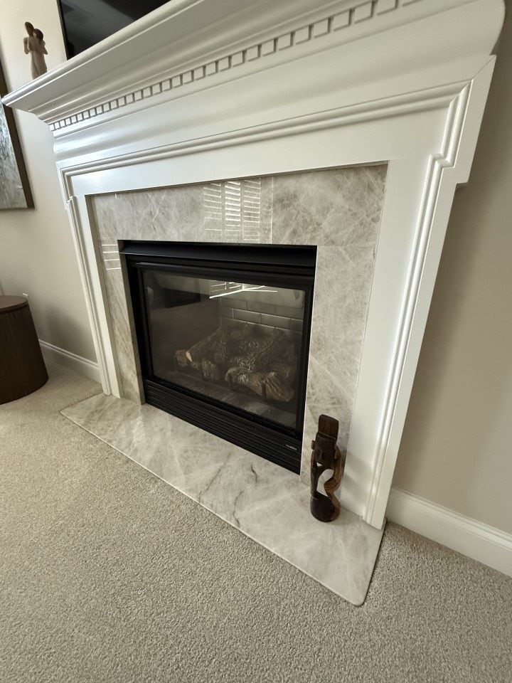White fireplace with marble tile surround, black glass front, and decorative object.