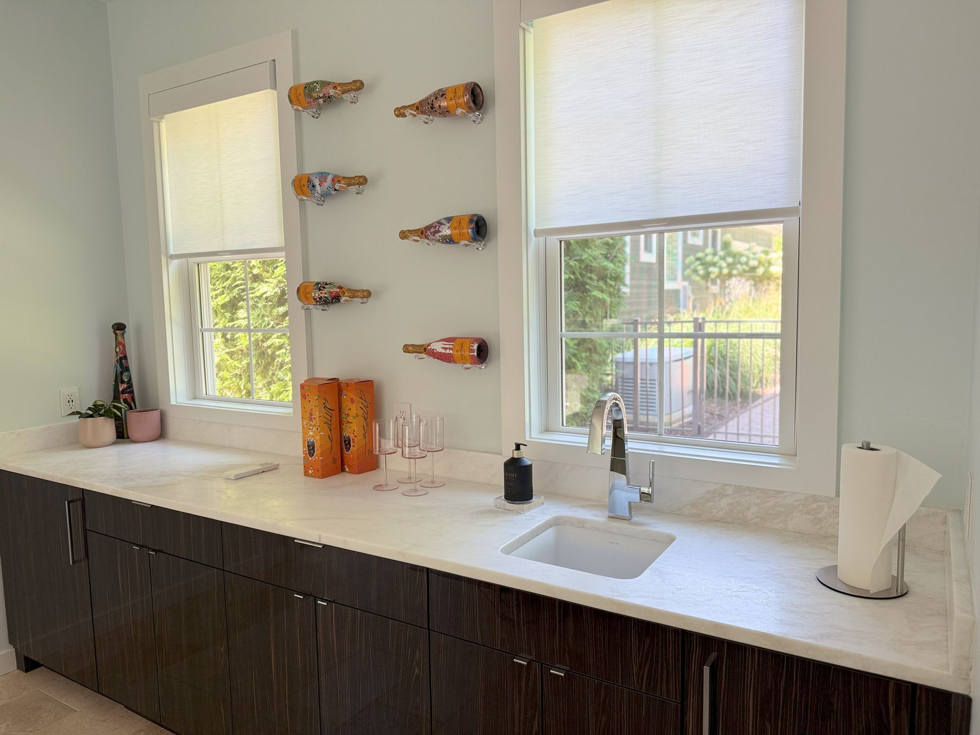 A bar area with windows, countertop, cabinets, a sink, and bottles mounted on the wall.