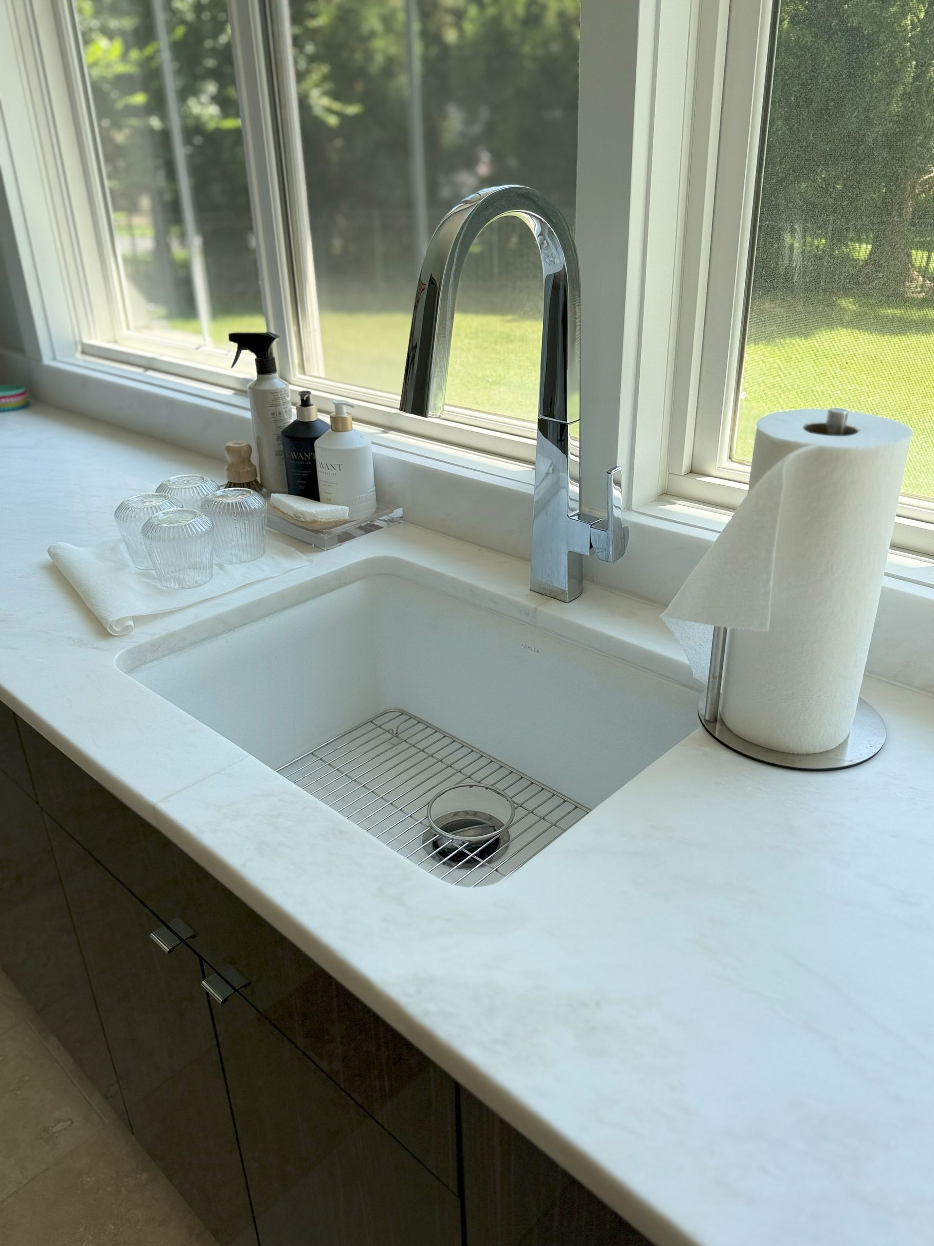 Kitchen sink with a high-arc faucet, paper towel holder, and a window overlooking a green yard.