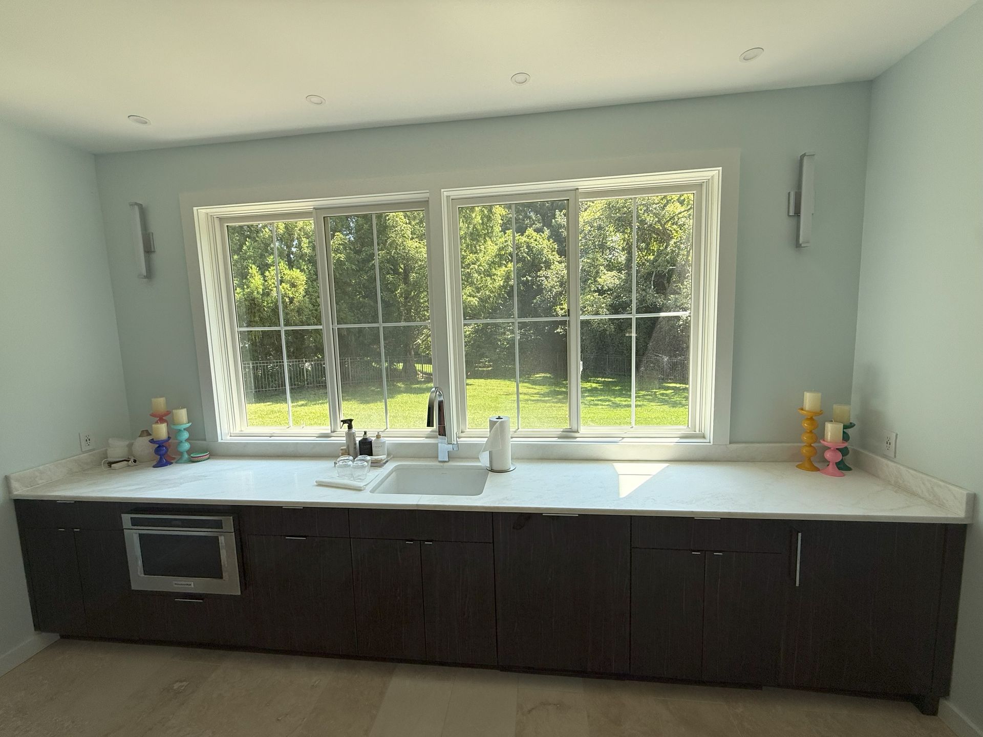 A laundry room with a dark brown cabinet below a white countertop and large windows.